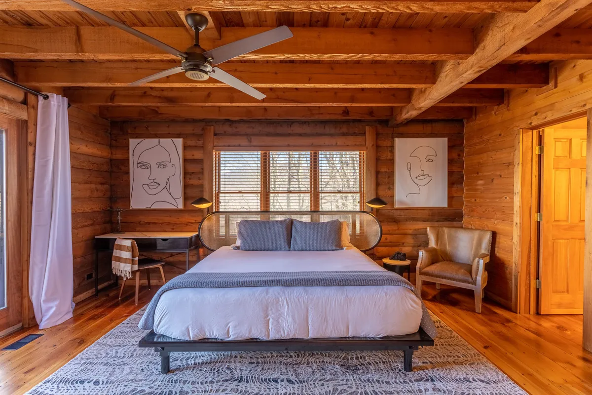 This image features a tranquil bedroom with a comfortable bed, tasteful artwork on the walls, a side table, and a cozy chair. Soft, natural light fills the space, creating a peaceful ambiance ideal for relaxation after a day of adventure.