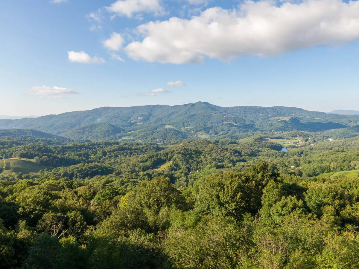 A breathtaking view of a mountain range under a blue sky, surrounded by lush greenery. The open vista inspires exploration and speaks to the outdoor adventure opportunities nearby.