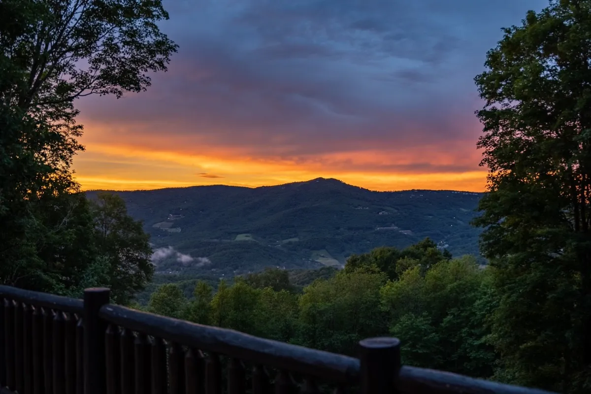 A breathtaking view of distant mountains under a dramatic sunset sky, framed by lush trees and scattered clouds. The scene evokes a sense of tranquility and grand scale, perfect for outdoor relaxation, photography, or sharing quiet moments with friends or loved ones.