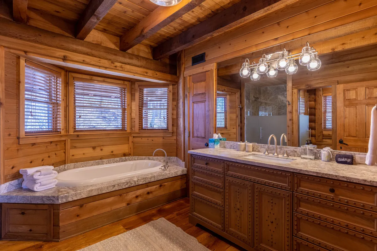 A luxurious bathroom showcasing a freestanding bathtub, double sink vanity, wooden cabinetry, and ample natural light streaming through the windows. The setting is spa-like and serene, ideal for unwinding.