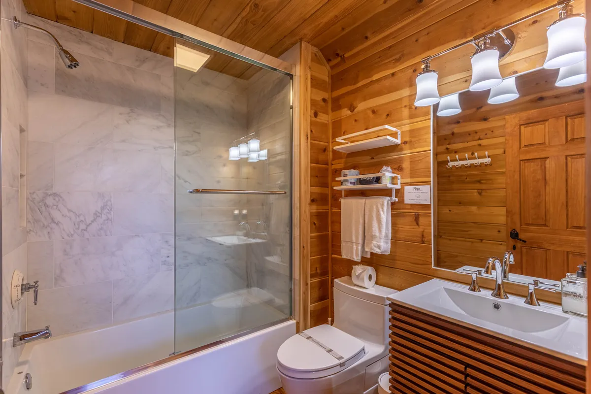 A modern bathroom with a glass-enclosed shower, dual sink vanity, and soothing wooden accents. The atmosphere is serene and designed for both relaxation and practical luxury.