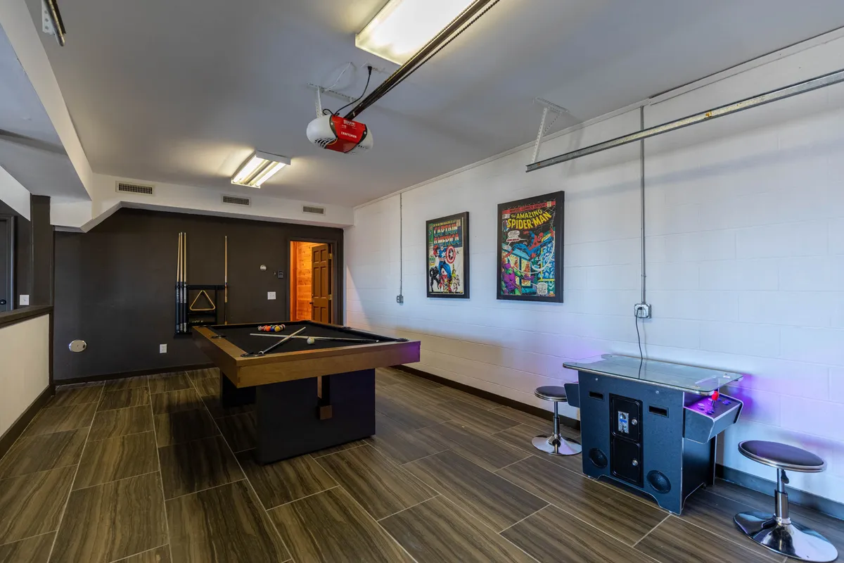 A lively game room with a sleek pool table in the center, bold comic book art decorating the walls, bar stools for spectators, and an entertainment unit featuring a television. The room invites both active fun and casual relaxation, perfectly suited for family tournaments and movie nights alike.