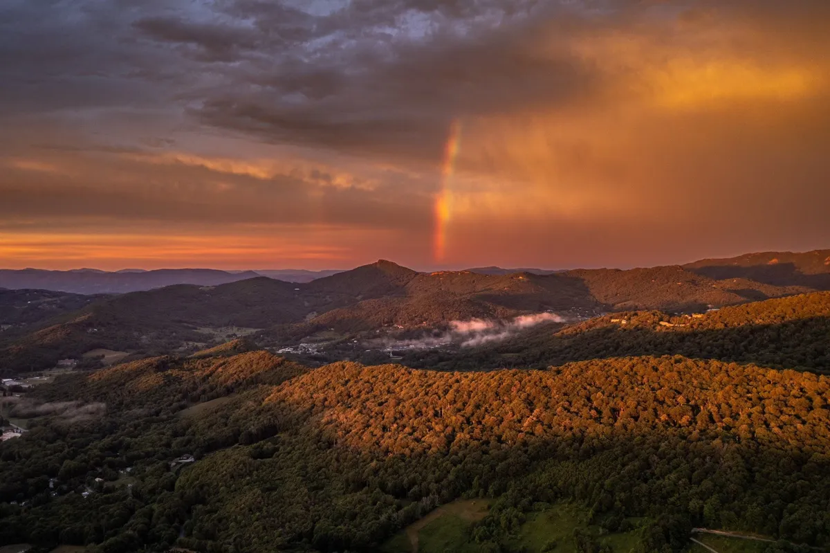 A breathtaking scenic view featuring a rainbow spanning a dramatic mountain range beneath a colorful sunset sky. The image captures the natural splendor and adventure awaiting just beyond the property.